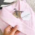 A hand holds a folded pink and white striped pyjama top with tags reading "British Boxers" and "Luscout Nightshirt M," perfect for pairing with a Satin Stripe Dressing Gown from British Boxers.