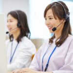 Two women wearing headsets and ID badges sit at desks in Texas, working on computers, possibly providing customer service or translation services.