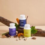 Three OSH Wellness supplement bottles are arranged on a log with various natural ingredients and leaves on a beige background, reflecting the care taken to choose quality supplements for your family's wellbeing.