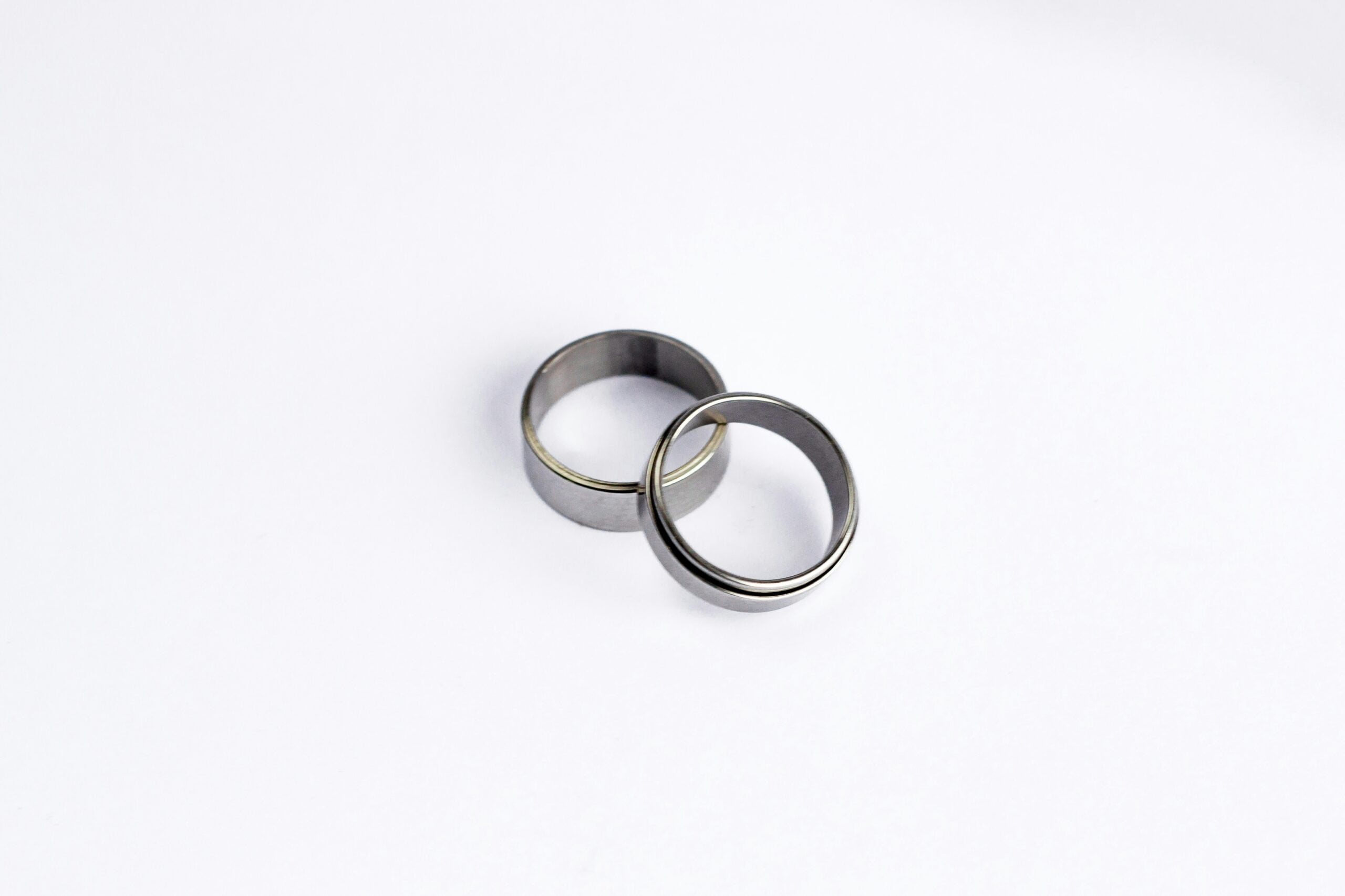 What Is a Pinky Promise Ring? Meaning, Symbolism, and Traditions Two plain silver rings rest on a white background, one slightly overlapping the other, evoking the symbolism of a pinkie promise ring and highlighting their deeper meaning.