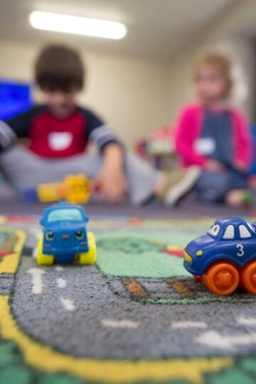 How Early Childhood Environments in River Oaks Shape the Way Children Learn to Think Two toy cars rest on a road-themed play mat in an Early Childhood Environments setting, whilst three children play together in the blurred background at River Oaks.