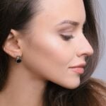 Woman in profile with long brown hair, wearing black and silver stud earrings, shows smooth skin and subtle make-up-an ideal reference for facelift planning in Philadelphia, looking slightly downward with a neutral expression.