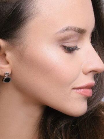 4 Things You Should Know Before Planning a Facelift in Philadelphia Woman in profile with long brown hair, wearing black and silver stud earrings, shows smooth skin and subtle make-up-an ideal reference for facelift planning in Philadelphia, looking slightly downward with a neutral expression.