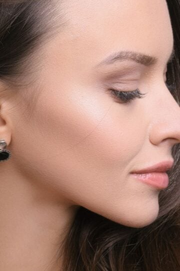 4 Things You Should Know Before Planning a Facelift in Philadelphia Woman in profile with long brown hair, wearing black and silver stud earrings, shows smooth skin and subtle make-up—an ideal reference for facelift planning in Philadelphia, looking slightly downward with a neutral expression.