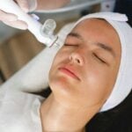 A person with a white headband receives a facial treatment with a handheld device, performed by someone wearing gloves-an ideal scene for those First Time Visiting a Medi Spa.