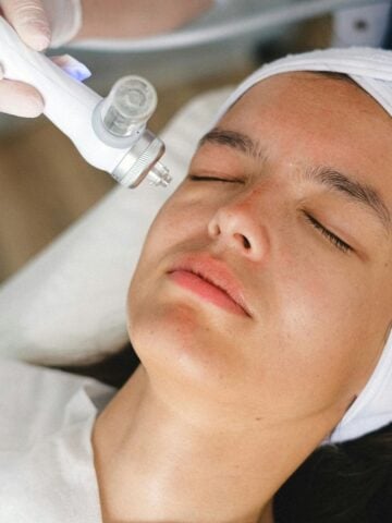 First Time Visiting a Med Spa? 4 Things You Should Prepare Your Mind For A person with a white headband receives a facial treatment with a handheld device, performed by someone wearing gloves-an ideal scene for those First Time Visiting a Medi Spa.
