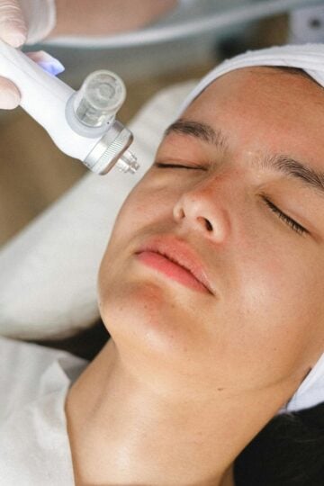 First Time Visiting a Med Spa? 4 Things You Should Prepare Your Mind For A person with a white headband receives a facial treatment with a handheld device, performed by someone wearing gloves—an ideal scene for those First Time Visiting a Medi Spa.