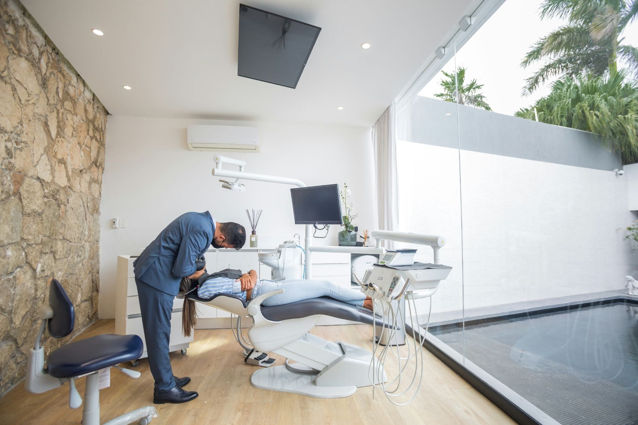 The Process Behind a Complete Dental Treatment Plan and What Patients Should Expect A dentist examines a patient lying in a dental chair inside a modern, bright dental surgery with large windows and a stone wall.