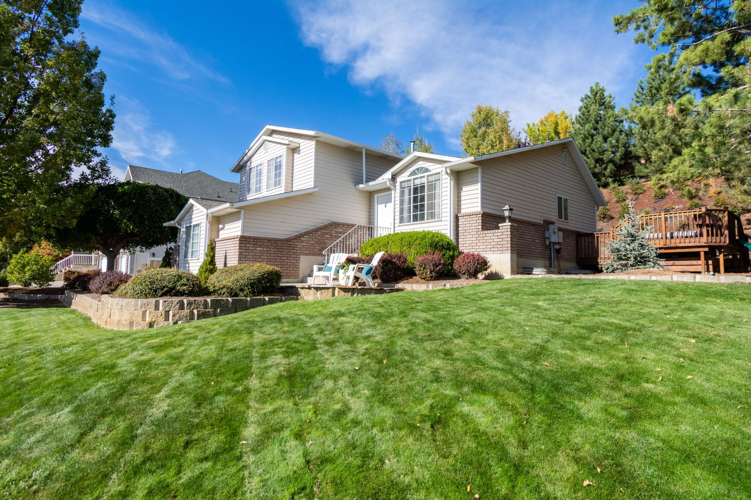 How Modern Homeowners Are Redefining What a Successful Landscape Looks Like Single-storey suburban house with beige cladding, brick accents, and manicured lawn on a sunny day; patio chairs and landscaped shrubs showcase successful garden ideas for modern homeowners.