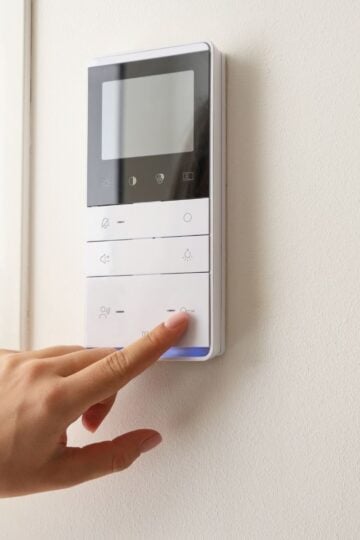 Enhancing Home Comfort and Efficiency A hand presses a button on a white wall-mounted control panel with a screen and several buttons.