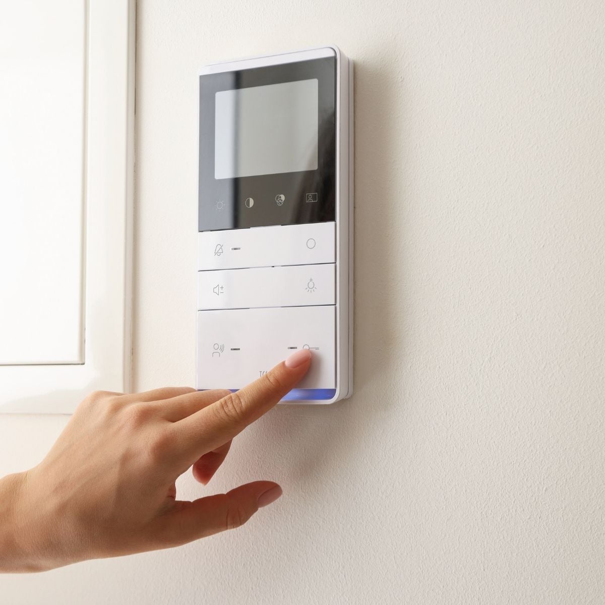 Enhancing Home Comfort and Efficiency A hand presses a button on a white wall-mounted control panel with a screen and several buttons.