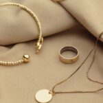 A gold bracelet, a plain gold ring, and a gold necklace with a round pendant are arranged on beige fabric-a perfect display for jewellery packing inspiration or handy jewellery travel tips.