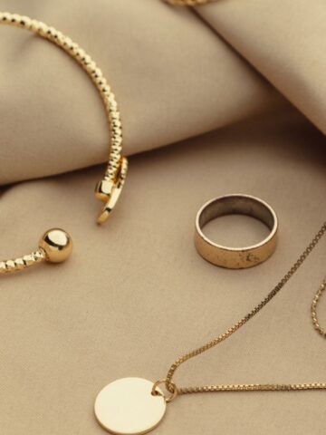 A gold bracelet, a plain gold ring, and a gold necklace with a round pendant are arranged on beige fabric-a perfect display for jewellery packing inspiration or handy jewellery travel tips.
