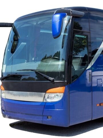 A blue coach with large windows is parked on a paved surface, photographed from the front left side against a white background-ideal for group travel or coach hire in Newcastle.