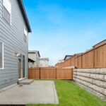 A small back garden with green grass, a concrete patio, a wooden fence installed by one of the top fencing companies Austin has to offer, and part of a grey two-storey house on the left under a clear blue sky.