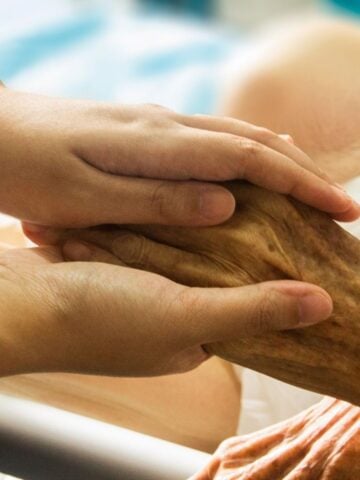 A younger person gently holds the hand of an older individual, showing support and care in a setting that appears to be a healthcare or hospital environment-highlighting the importance of palliative care in improving quality of life after a major stroke.