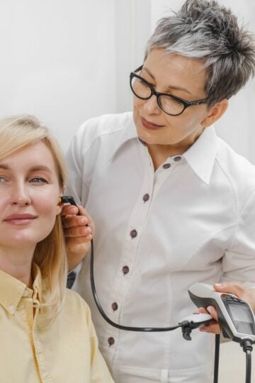 A healthcare professional examines a patient’s ear using an otoscope in a medical surgery setting.