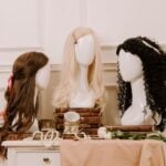 Three mannequin heads with wigs-brown, blonde, and black curly-are displayed among stacked