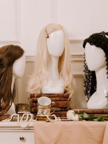 Three mannequin heads with wigs-brown, blonde, and black curly-are displayed among stacked