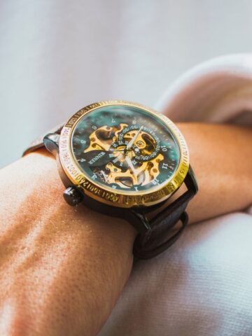 A close-up of a wrist wearing a mechanical watch with visible gears, a gold bezel, and a brown leather strap, showcasing the timeless style that defines luxury watches and their generational appeal.