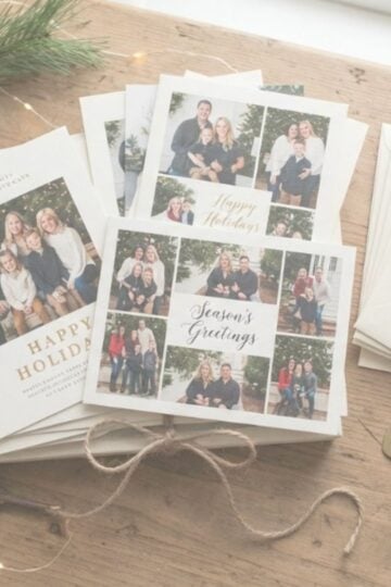 A stack of holiday greeting cards with family photos, inspired by the best Holiday photo card sites for the 2026 season, sits on a wooden table beside envelopes, a bottle opener, and pine cone decorations.