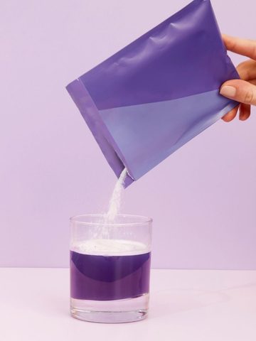 Hydrolyzed Bovine Collagen Peptides: An Easy Addition to Everyday Wellness A hand pours white powder from a purple packet of Collagen Peptides into a clear glass containing purple liquid, against a light purple background.
