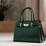 A dark green leather handbag with gold hardware sits on a light-coloured surface, with a blurred background-an elegant choice for those who appreciate vintage bags and timeless style.