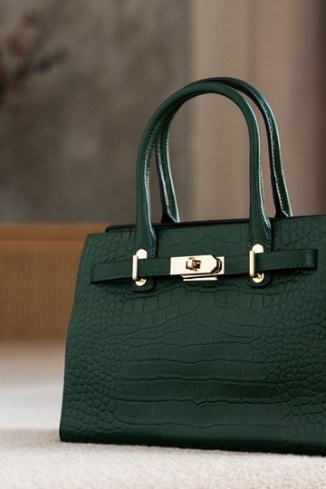 A dark green leather handbag with gold hardware sits on a light-coloured surface, with a blurred background—an elegant choice for those who appreciate vintage bags and timeless style.