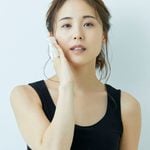 Woman in a black vest holds a white facial pad to her cheek, looking forward with a neutral expression against a plain light background-a simple moment that highlights the importance of skincare toners in everyday skincare routines.