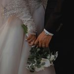 The Details That Make a Wedding Feel Truly Personal Close-up of a couple holding hands, one in a white, beaded dress holding a bouquet, the other in a black suit wearing a watch and wedding ring.